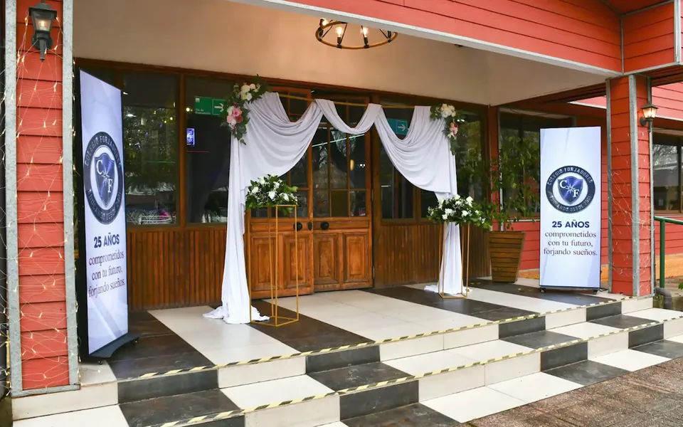 Entrada del colegio decorada con cortinajes blancos y flores para la ceremonia de los 25 años